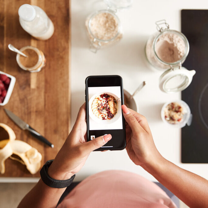 Overhead Shot Of Woman Taking Picture Of Healthy Breakfast On Mobile Phone At Home After Exercise